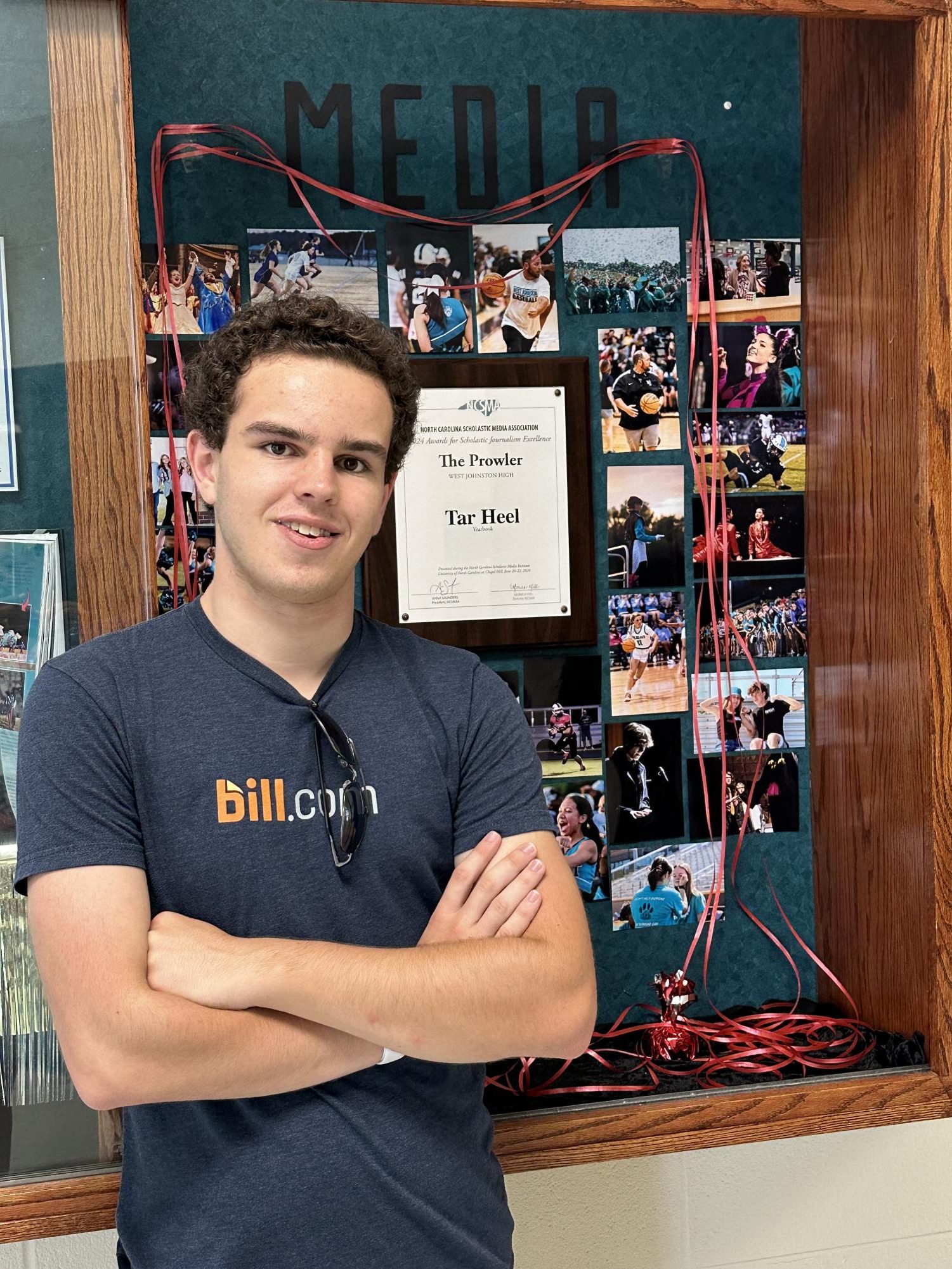 Connor Ruesch, Editor-in-Chief, The Prowler poses in front of the WJ Student Media showcase. Ruesch created a collage of yearbook photos and mounted the publication’s recent Tar Heel award. 
